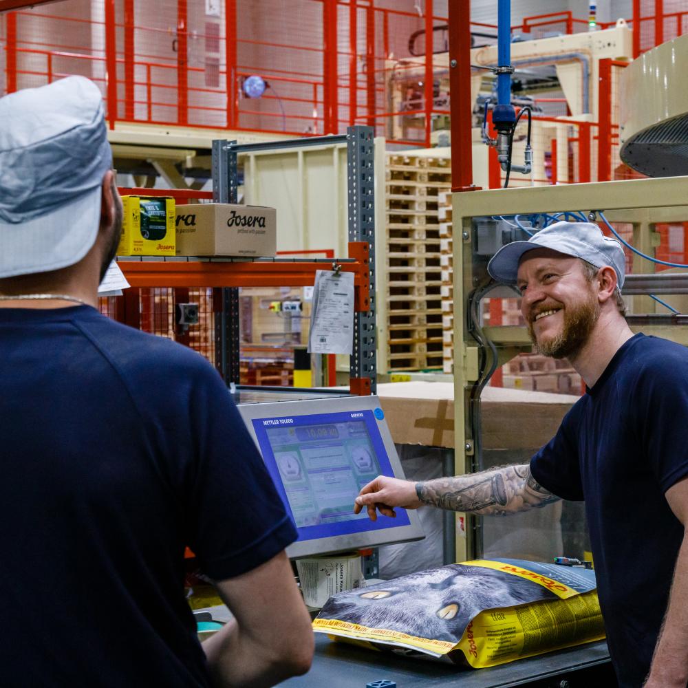Zwei Mitarbeiter in der Produktion lächeln sich bei der Arbeit an.